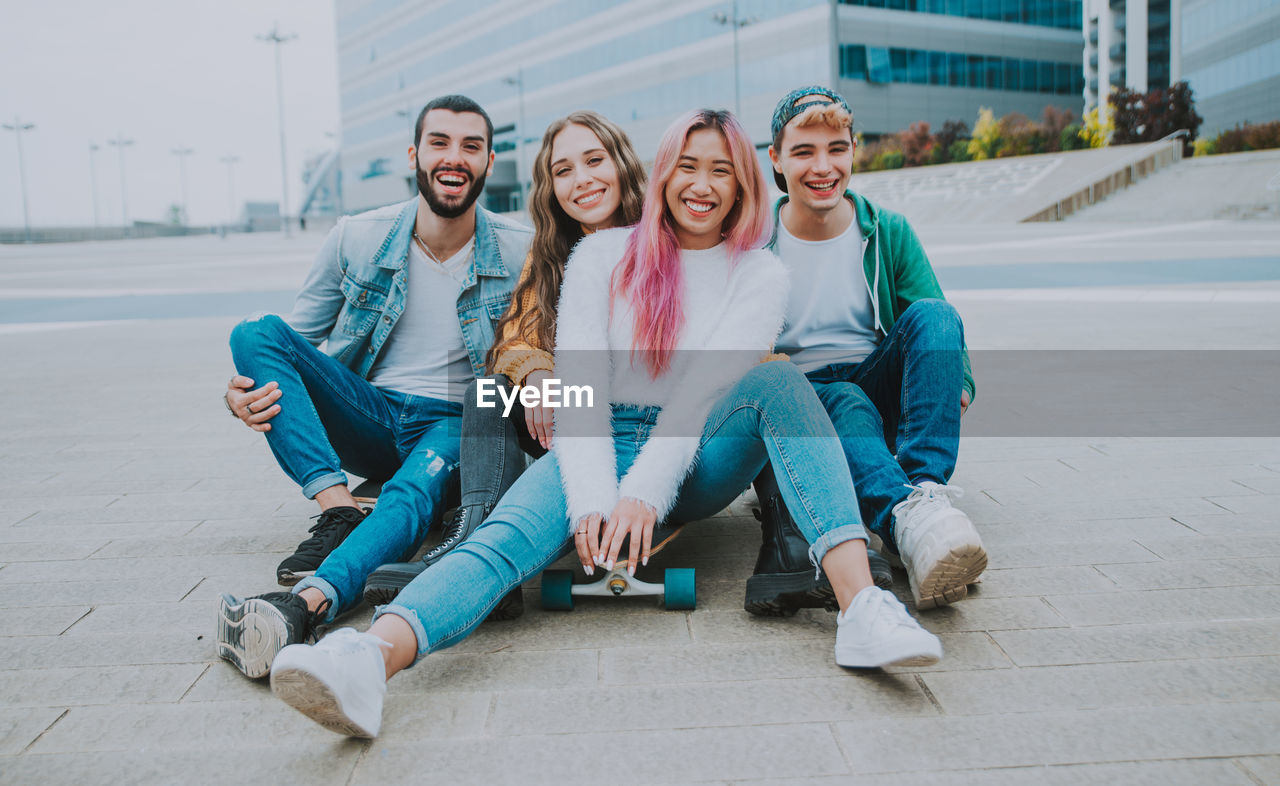 Portrait of cheerful friends sitting against building outdoors