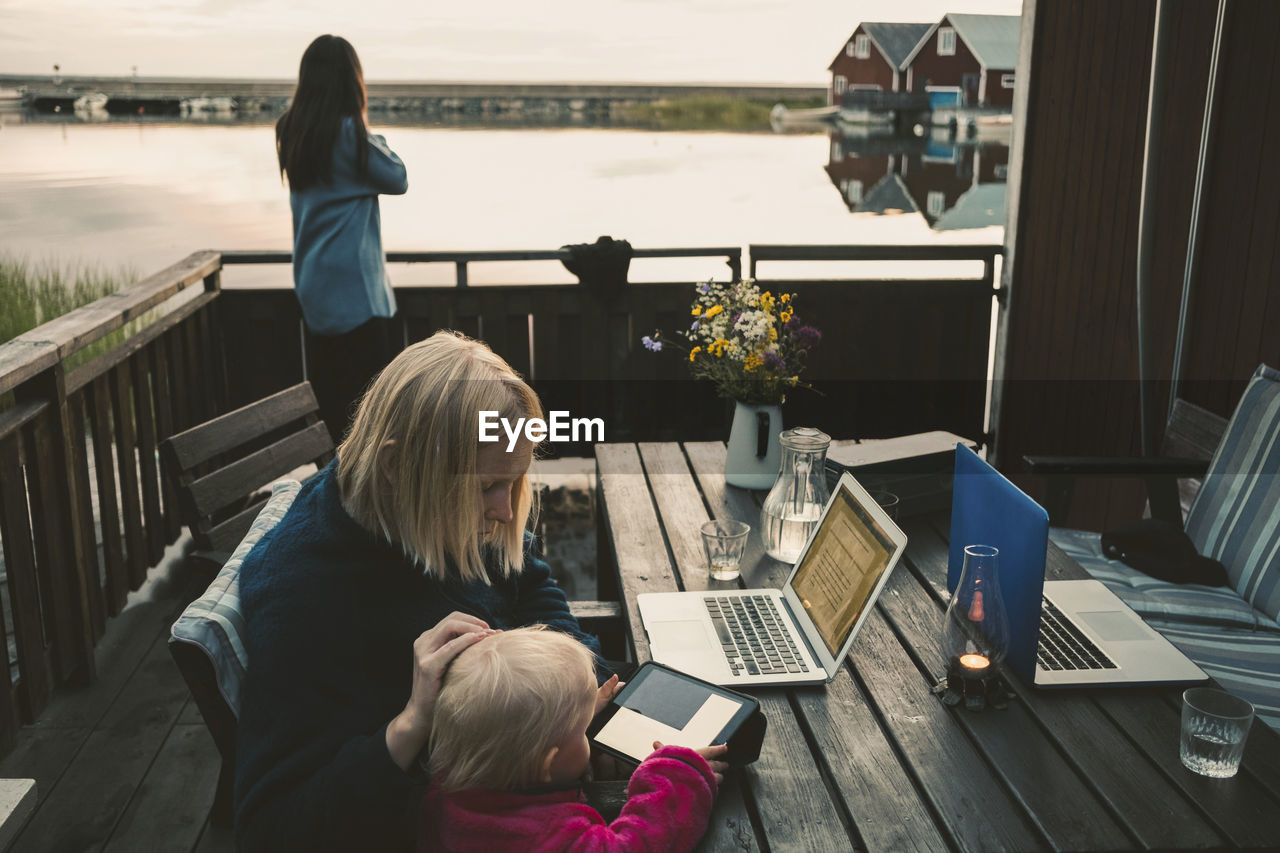 Woman teaching daughter in using digital tablet while friend talking on mobile phone
