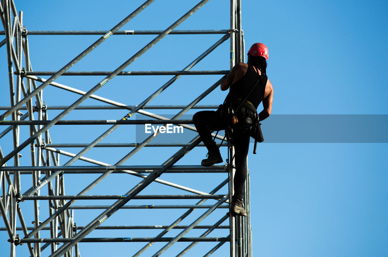 LOW ANGLE VIEW OF MAN WORKING AT CONSTRUCTION SITE AGAINST CLEAR SKY