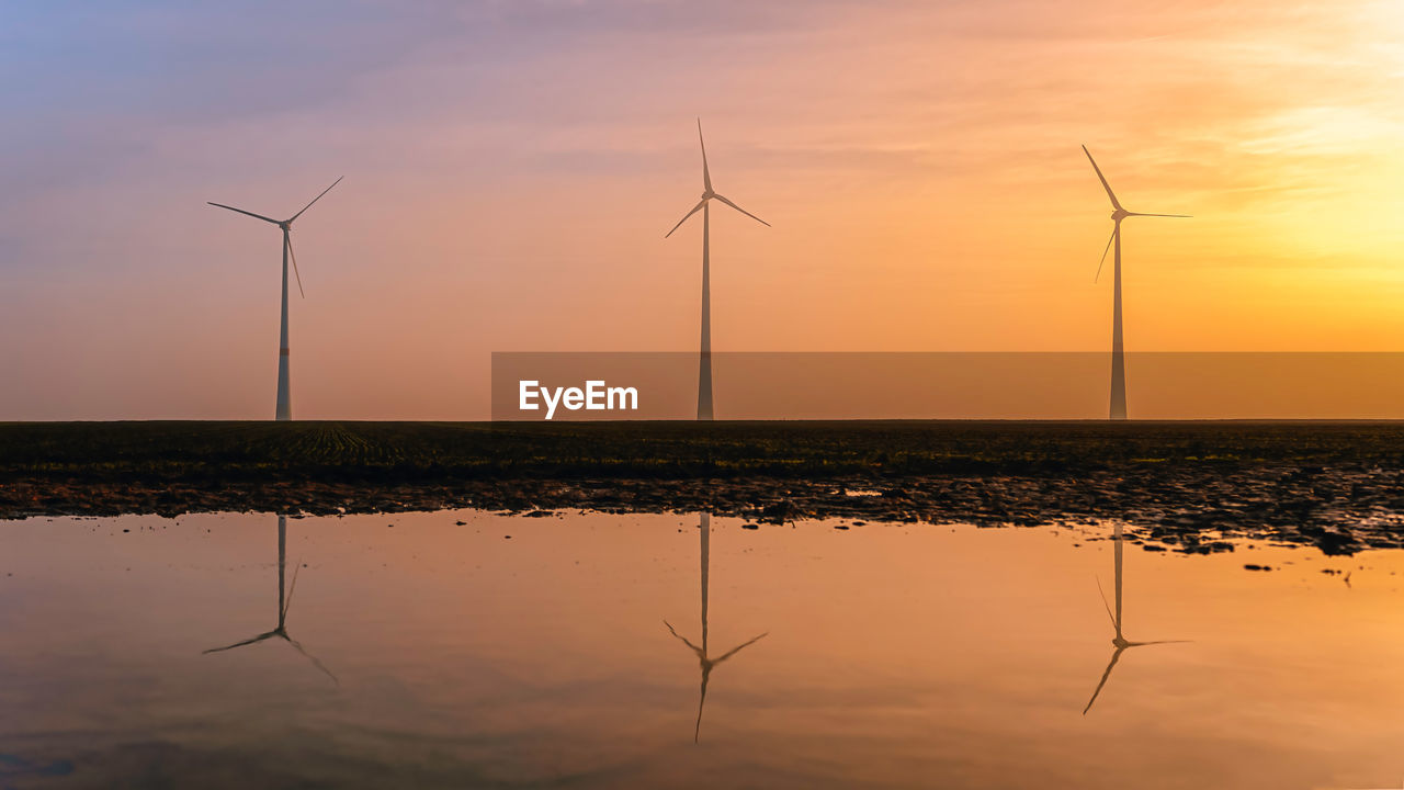 Wind turbines on the field reflecting in water under the sky during sunset