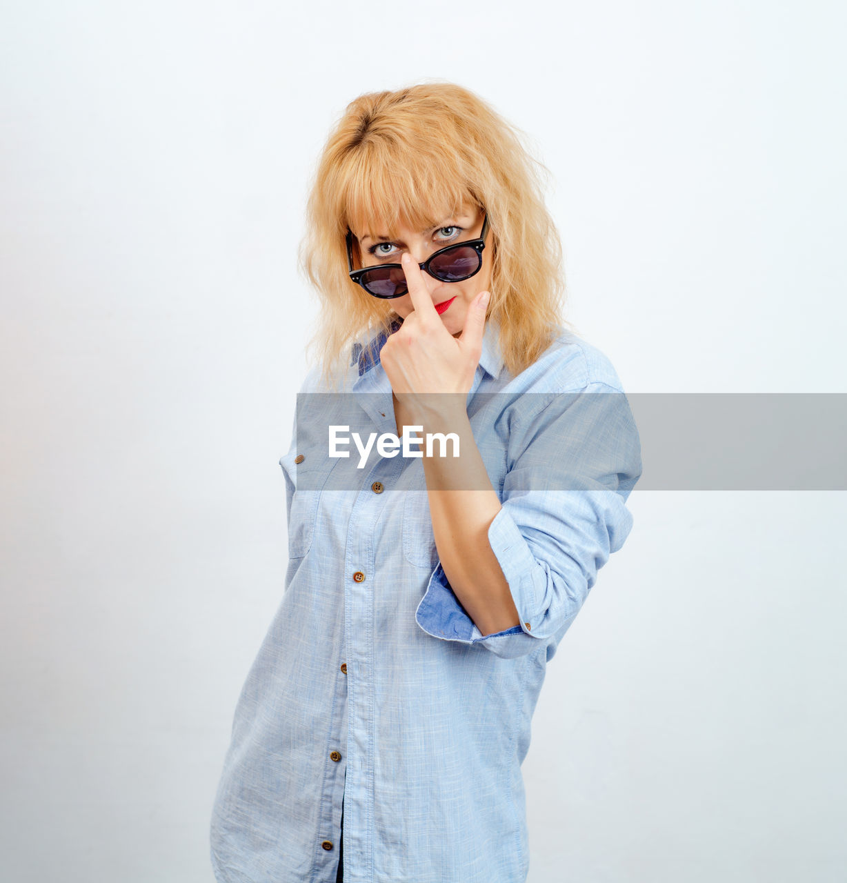 Blonde woman looks at camera through lowered glasses. female curiosity.