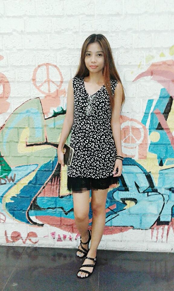 YOUNG WOMAN STANDING AGAINST WALL