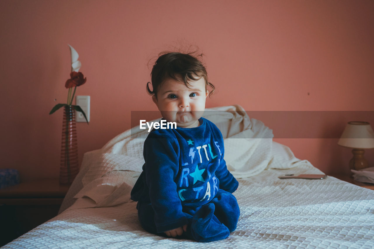 Portrait of boy sitting on bed at home