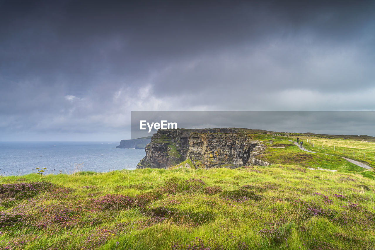 sky, coast, sea, land, cloud, water, cliff, grass, nature, beach, scenics - nature, horizon, environment, beauty in nature, plant, landscape, ocean, hill, coastline, travel destinations, shore, overcast, terrain, rock, no people, storm, travel, architecture, horizon over water, tranquility, tourism, history, storm cloud, outdoors, tranquil scene, non-urban scene, dramatic sky, the past, green, day, seascape, built structure, old ruin, island, cloudscape, building, highland, holiday, trip, idyllic