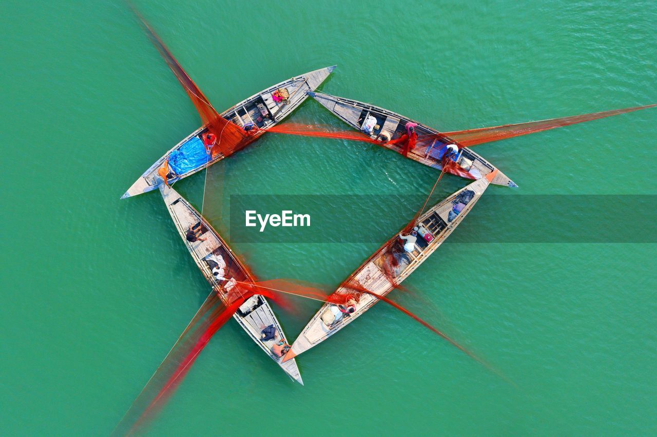 Fishermen draw their boats together so they can help each other lower a large net into the water. 
