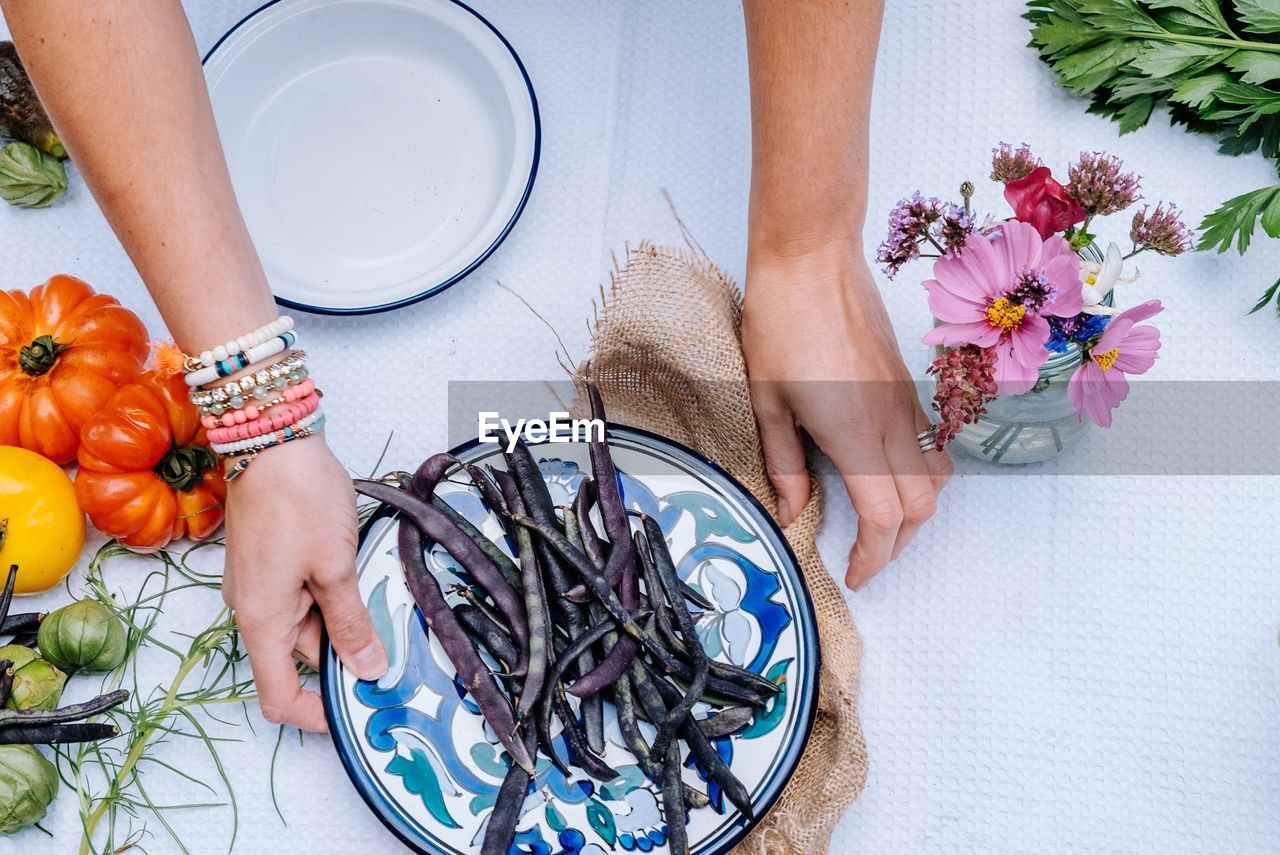 Cropped hands of woman with beans and flowers on table