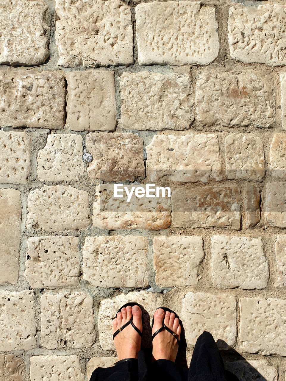 shoe, low section, one person, human leg, wall, standing, personal perspective, brick, lifestyles, architecture, day, limb, human limb, adult, stone wall, sandal, wall - building feature, human foot, leisure activity, brick wall, outdoors, women, built structure, men, sunlight
