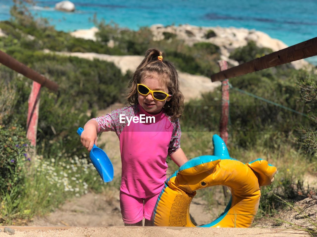 Girl wearing sunglasses while holding inflatable ring and toy at beach