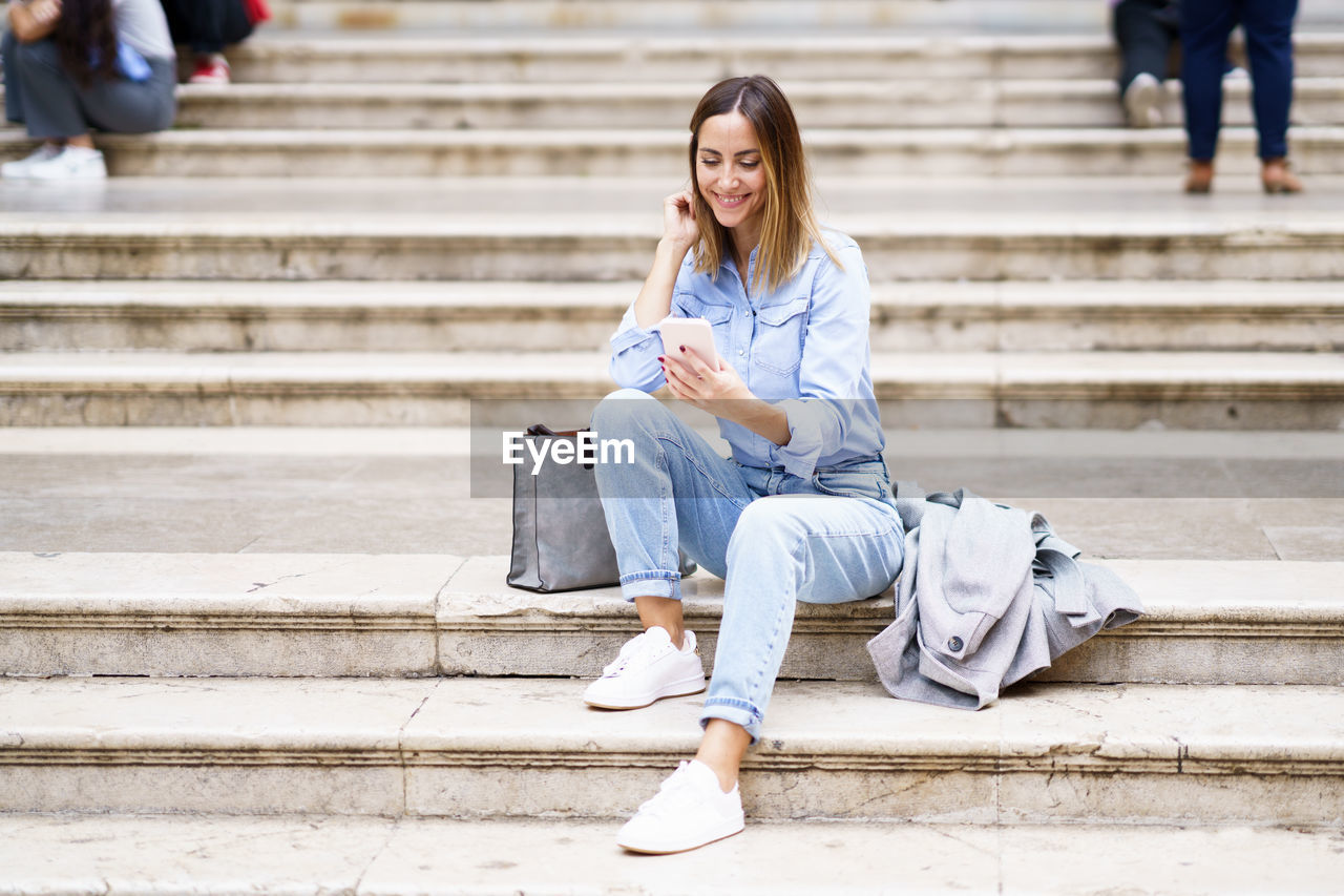 young woman using mobile phone while sitting on steps