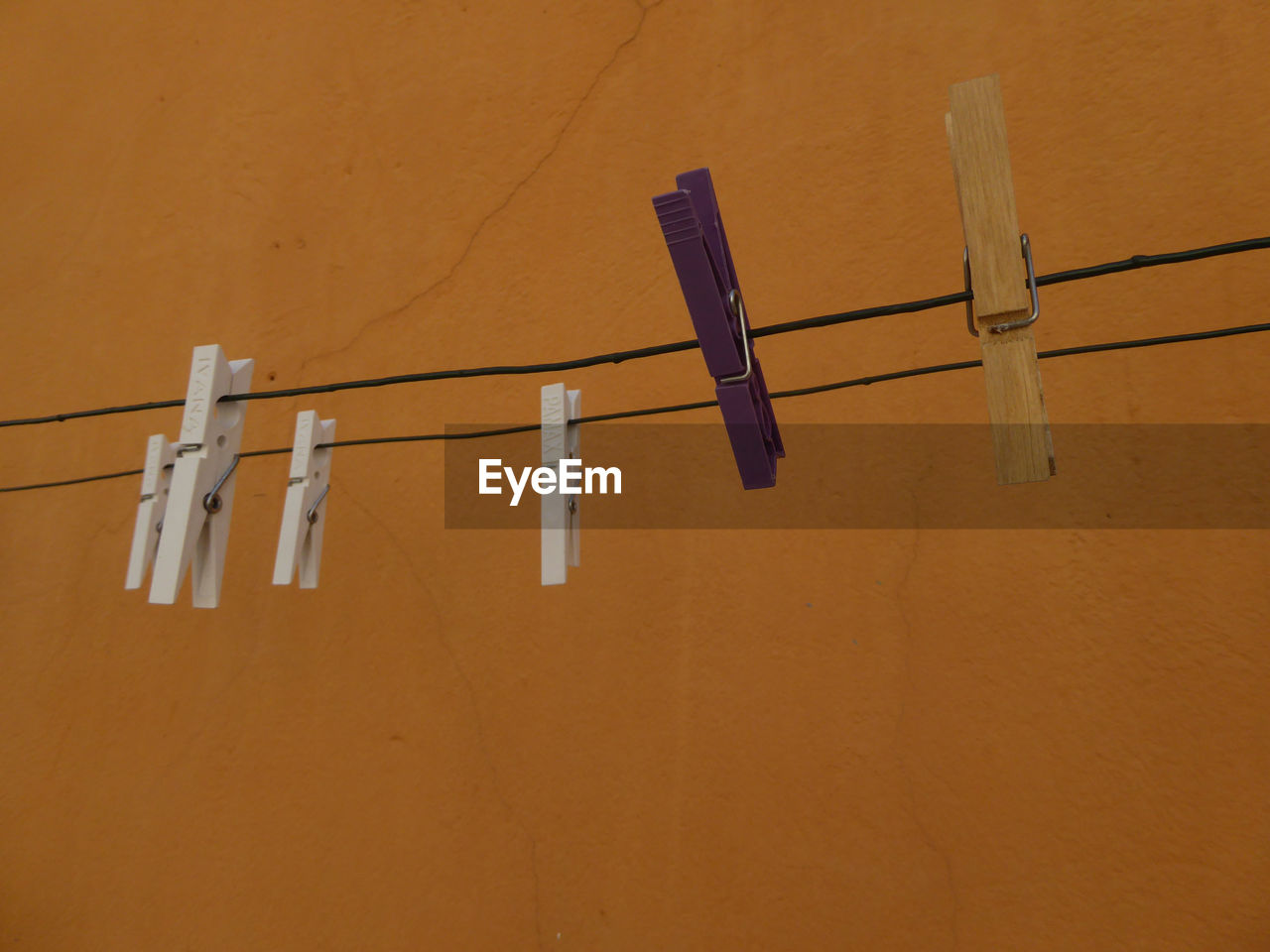 clothesline, hanging, clothespin, laundry, drying, no people, line, wing, wall - building feature, wood, in a row, group of objects, wall, coathanger, clothing, rope, indoors, lighting, yellow