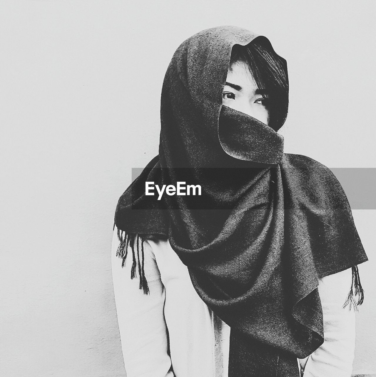 Young woman covering face with scarf against white background