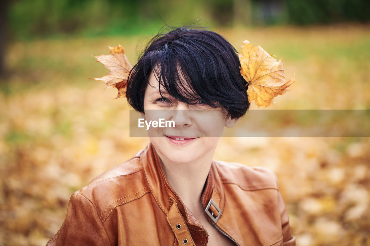 Portrait of smiling woman with autumn leaves on head