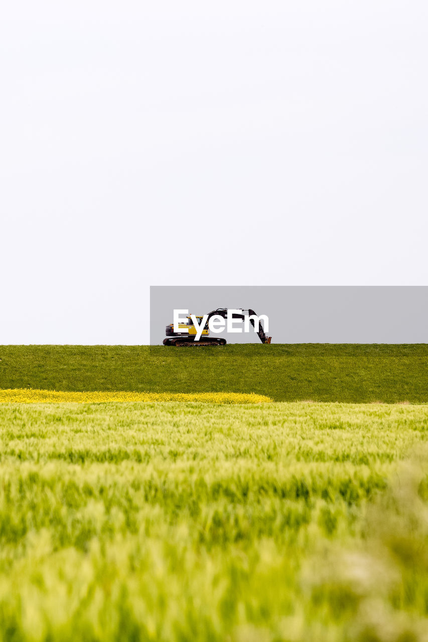Earth mover on grassy field against clear sky