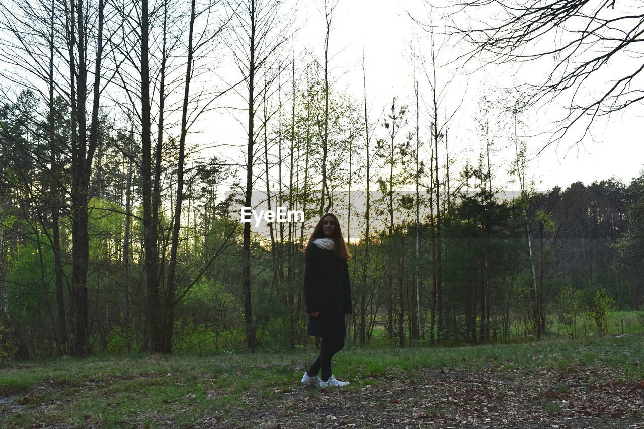 Full length of woman standing on field in forest