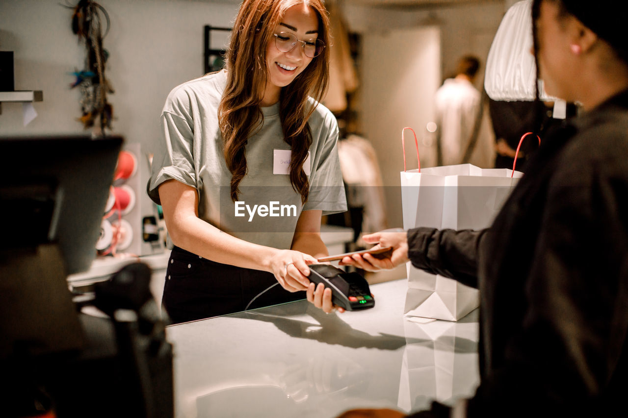 Female customer paying through smart phone to smiling saleswoman at store