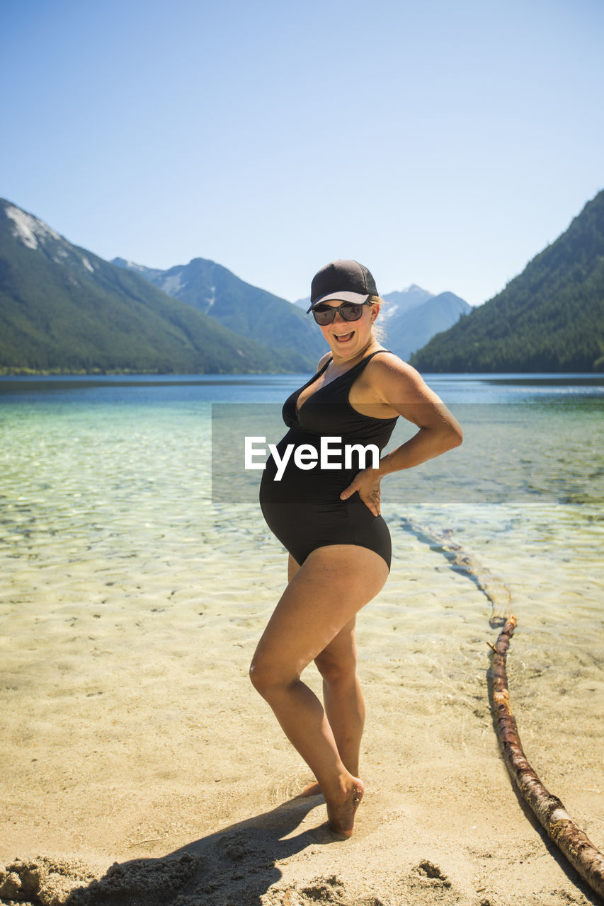 Portrait of pregnant woman rocking baby belly at the beach.