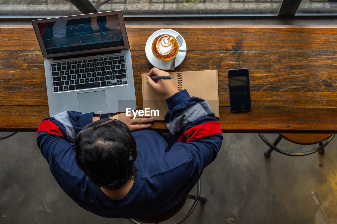 rear view of man using mobile phone while sitting on table