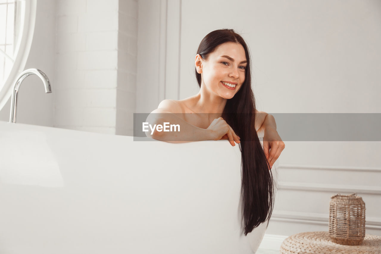 PORTRAIT OF SMILING YOUNG WOMAN SITTING ON TABLE