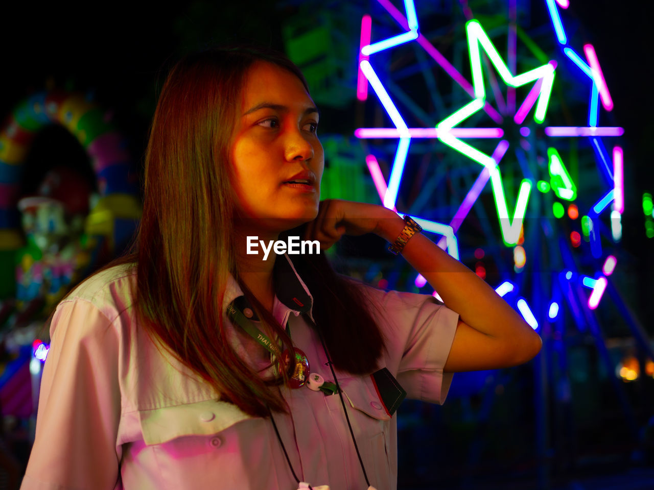 Woman looking away while standing against illuminated ferris wheel at night