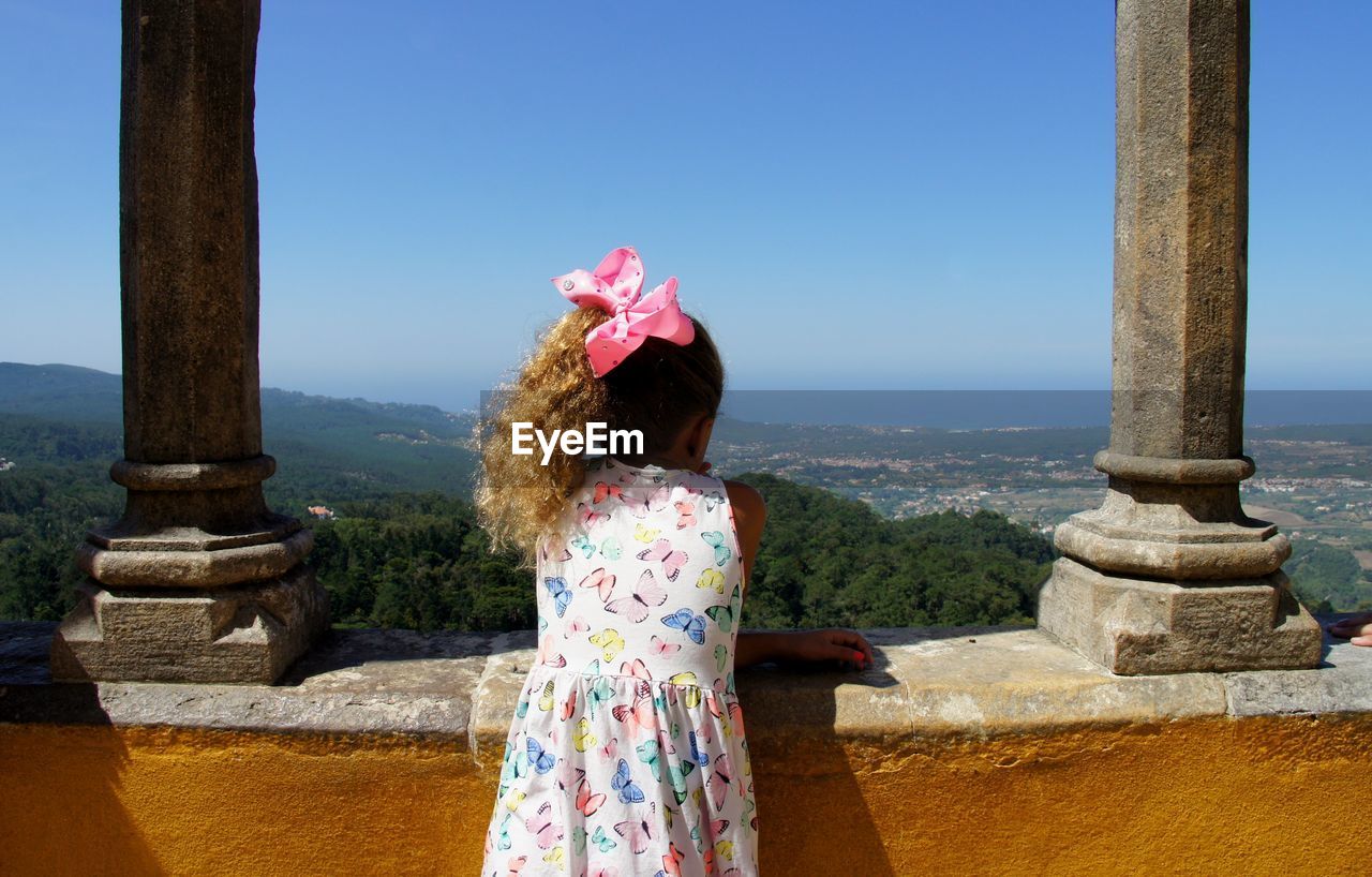 Rear view of girl standing by retaining wall against clear sky