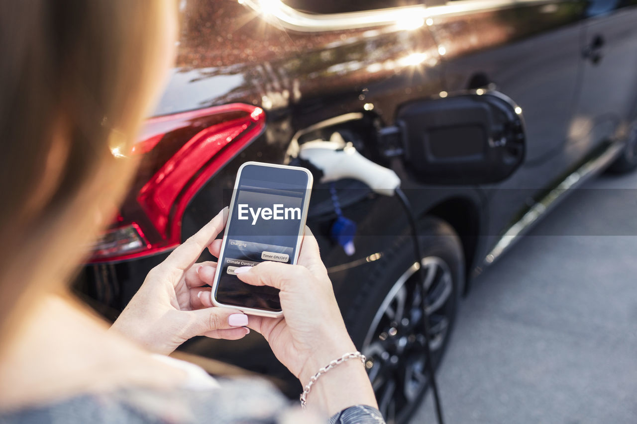 Woman using smart phone while standing by charging electric car