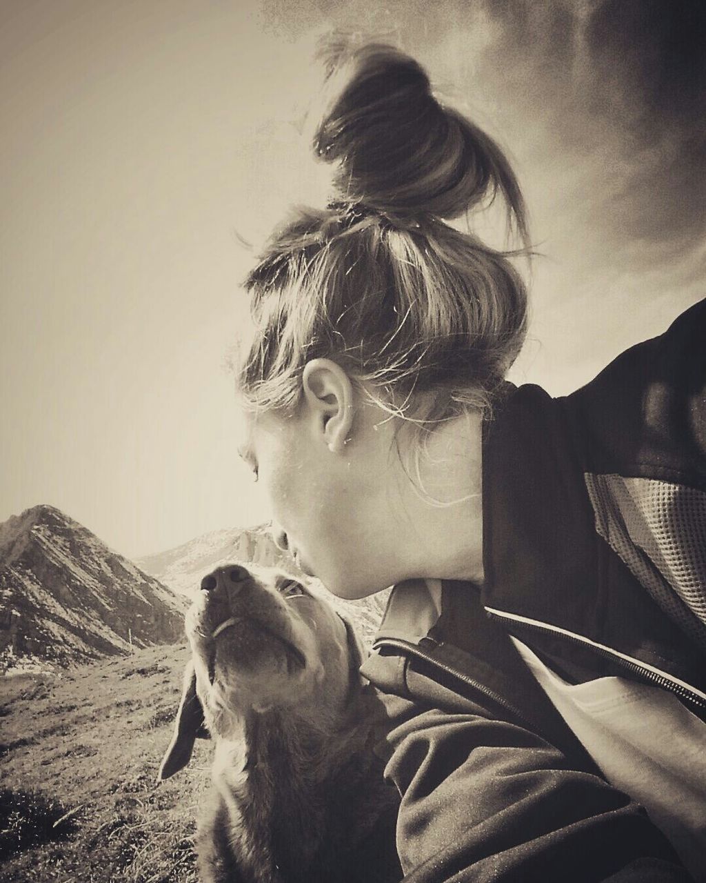 Young woman sitting by dog on mountain against sky