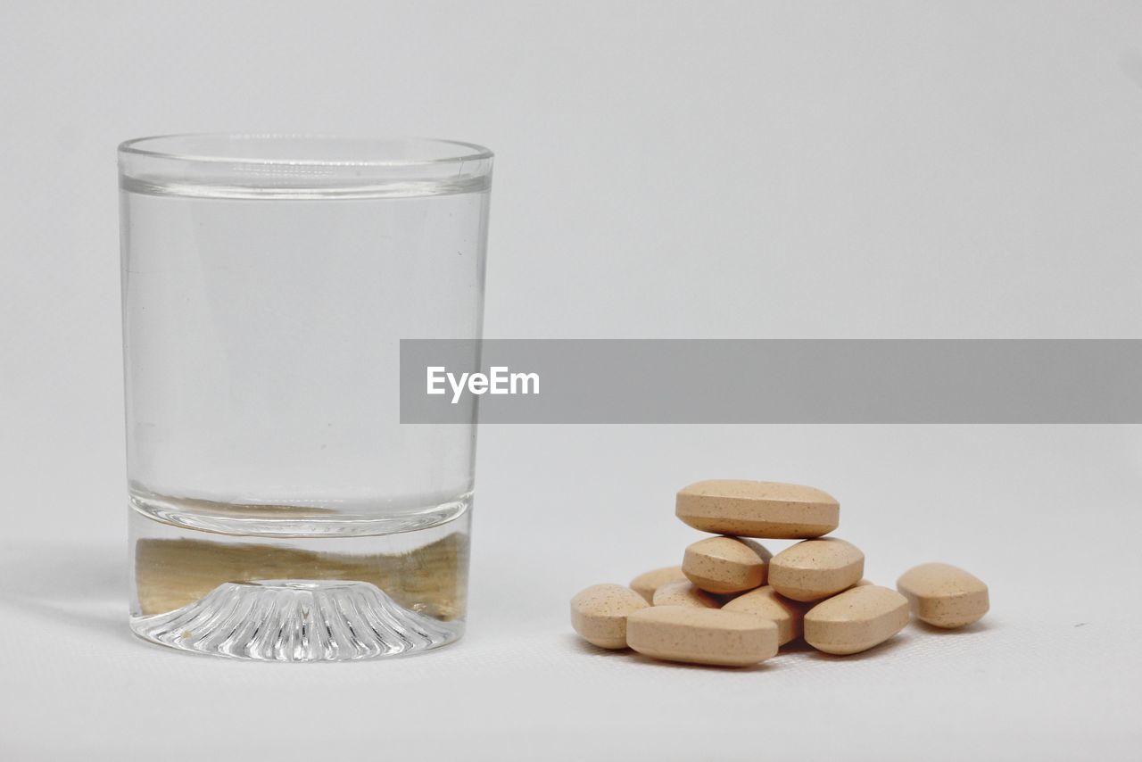 Close-up of water and pills against white background