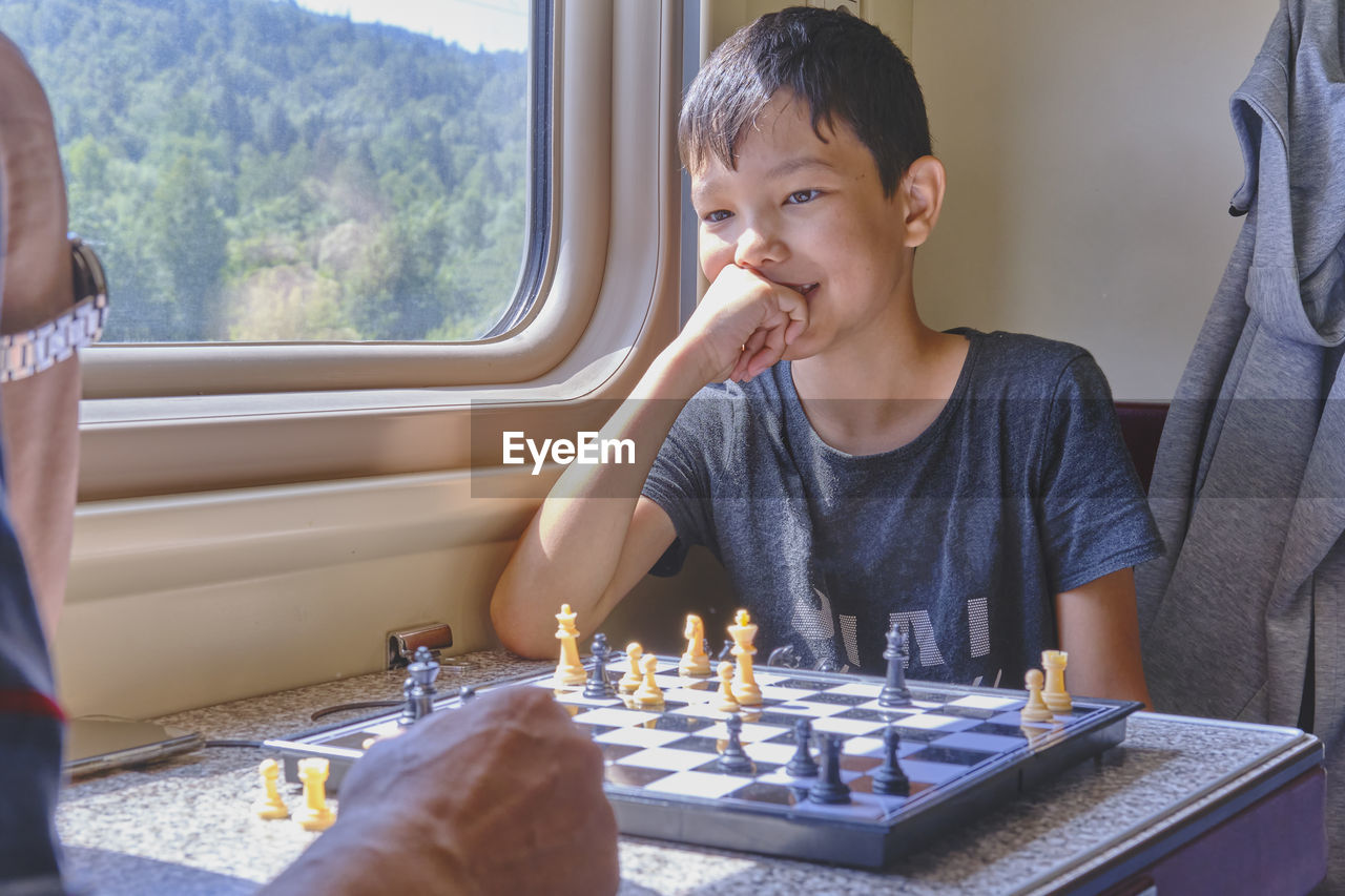 Asian boy smiling and playing chess in the train travel, table games concept