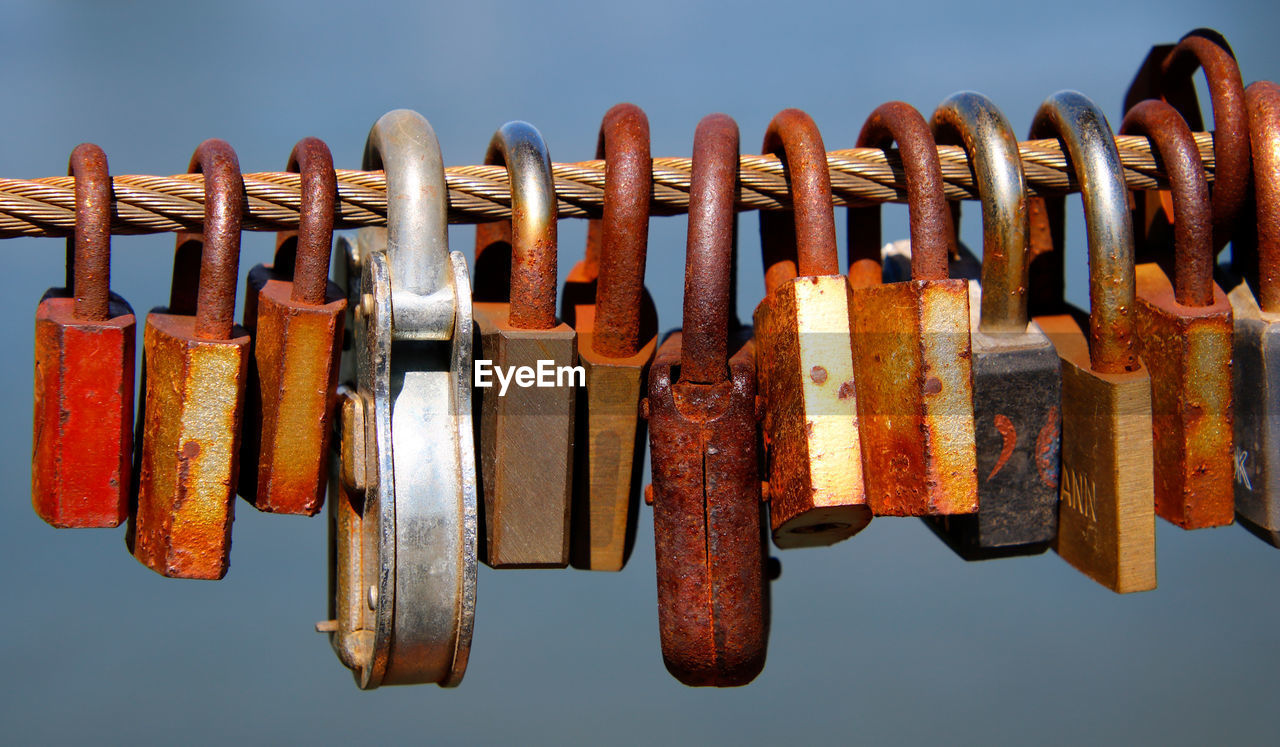 Close-up of padlocks hanging on rusty metal cable against sky