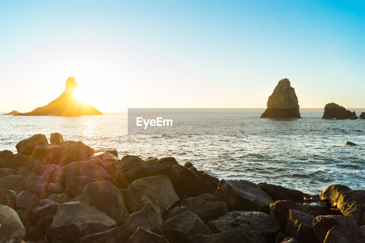 ROCKS ON SEA SHORE AGAINST CLEAR SKY