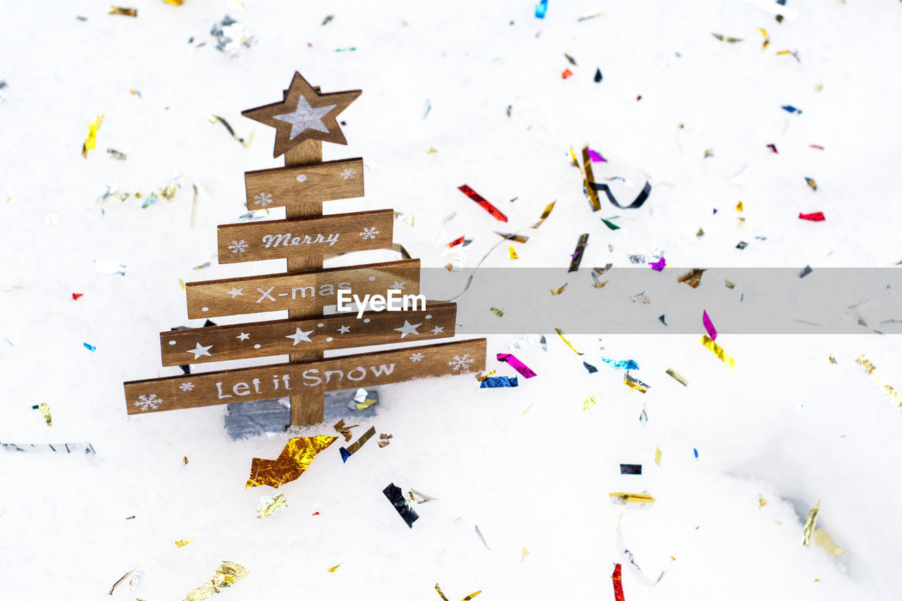 High angle view of wooden christmas tree with confetti over white background