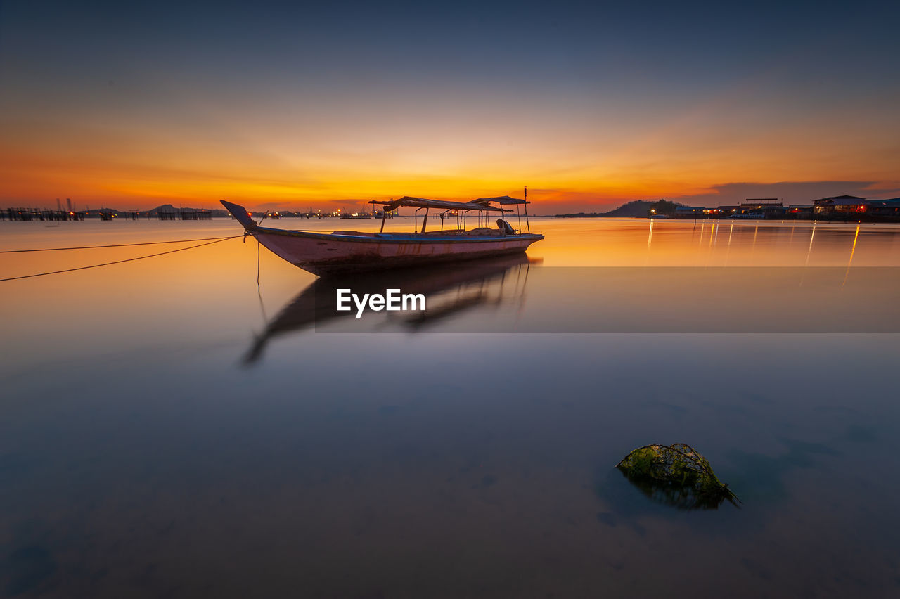 Boat moored in sea against sky during sunset