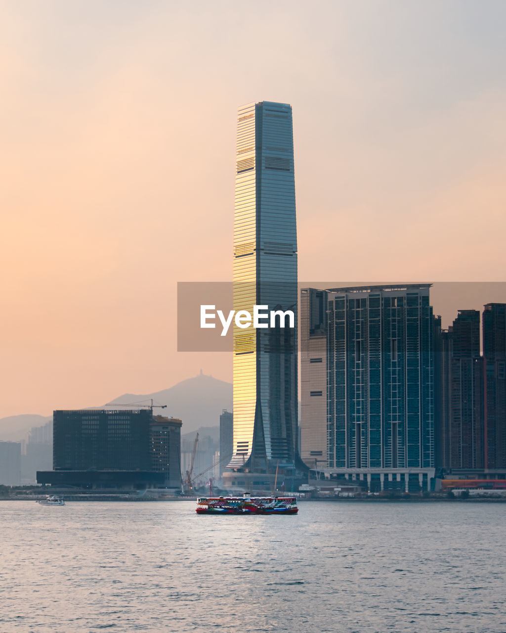 Sea by modern buildings against sky during sunset