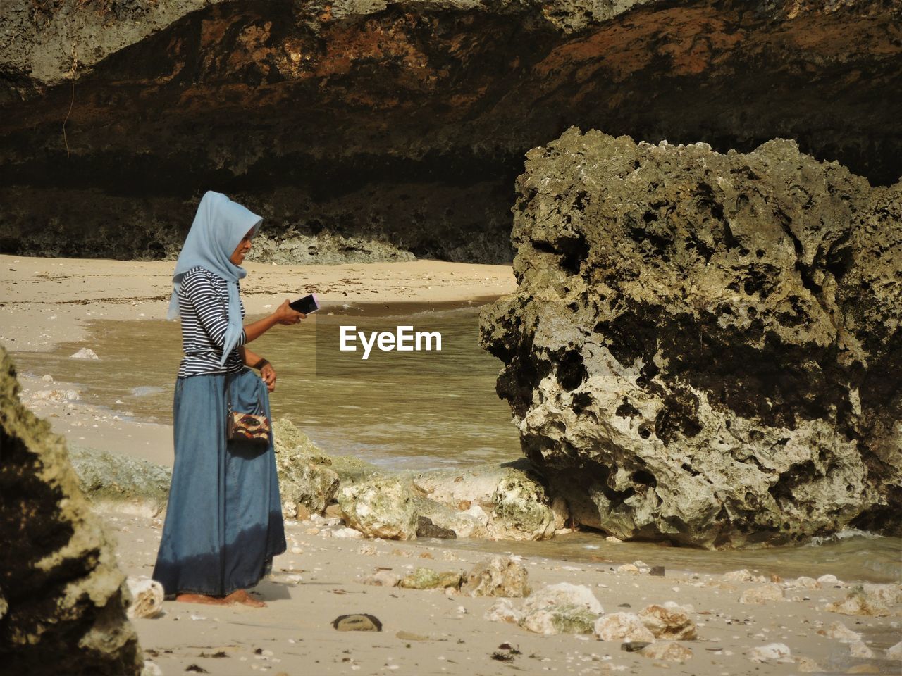 WOMAN HOLDING UMBRELLA STANDING ON ROCK FORMATION IN WATER