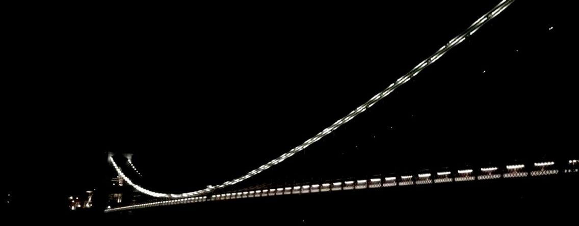 LOW ANGLE VIEW OF ILLUMINATED BRIDGE AT NIGHT