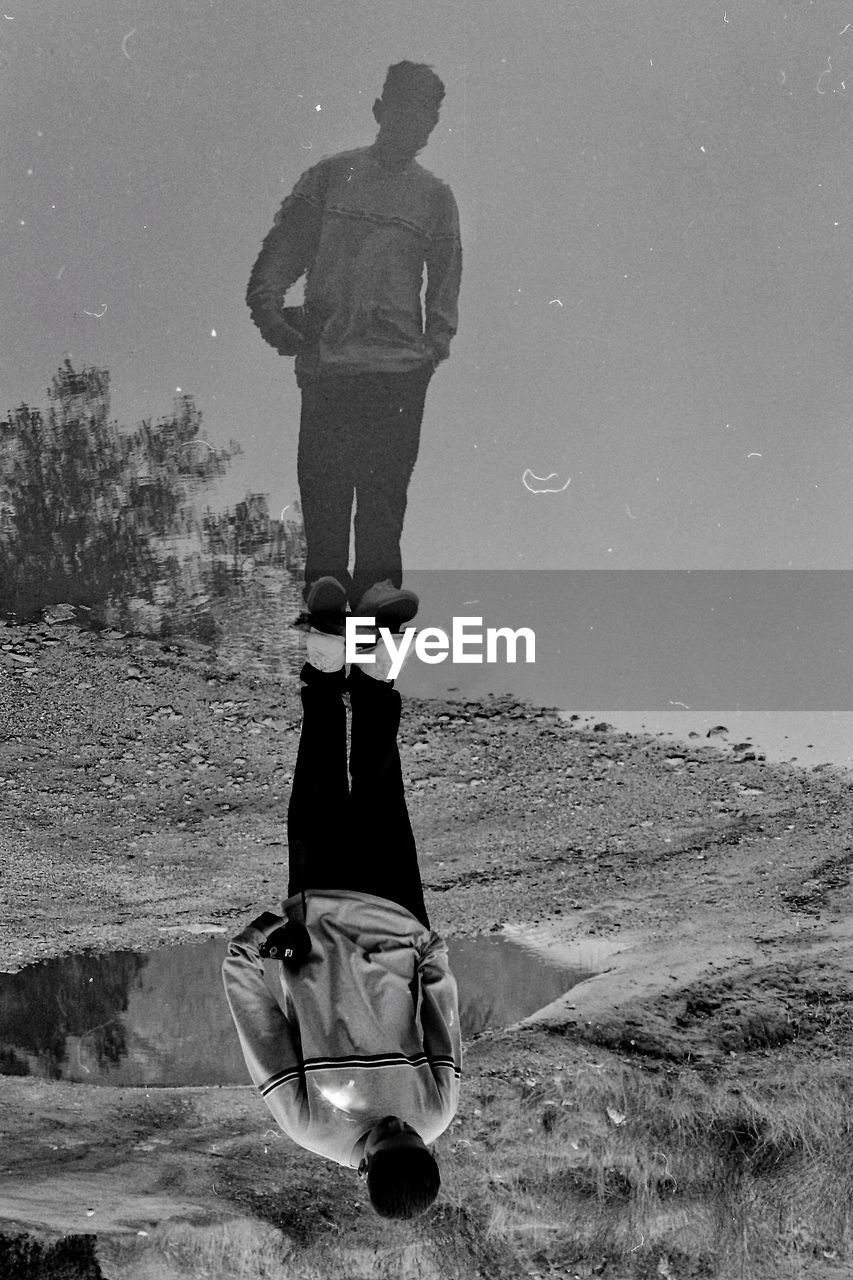 Upside down image of man reflecting in puddle on field during rainy season