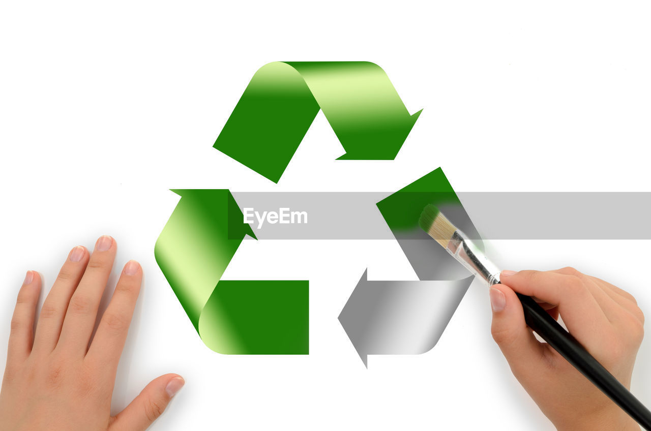 Cropped hand of person painting recycling symbol against white background
