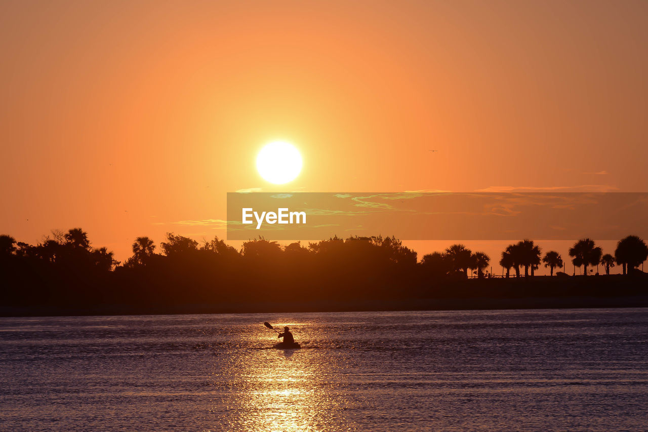 Silhouette man paddleboarding on sea against sky during sunset