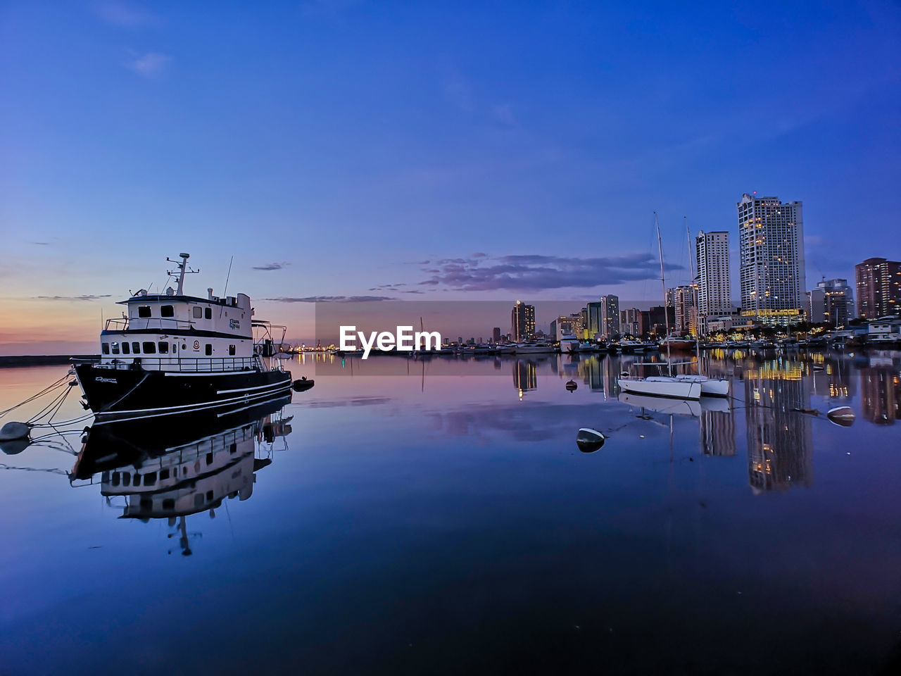 BOATS MOORED ON RIVER BY BUILDINGS IN CITY AGAINST SKY