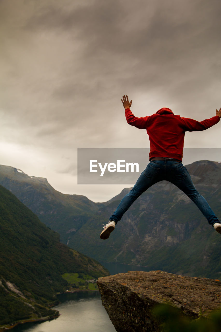 Rear view of man jumping on mountain against sky