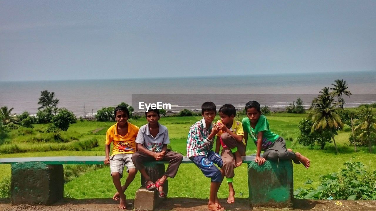 FULL LENGTH OF FRIENDS STANDING ON SEA SHORE AGAINST SKY