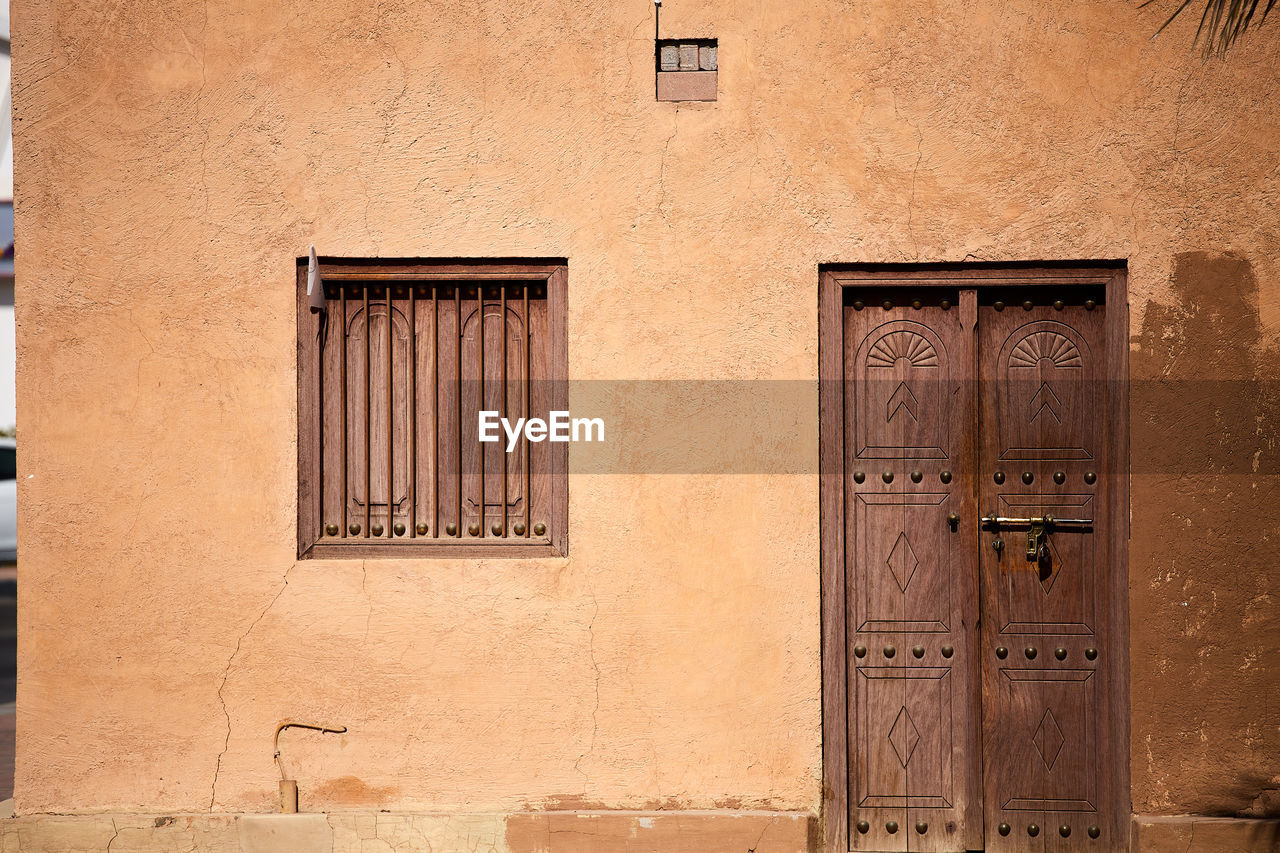 A weathered exterior house wall, with a closed window and door