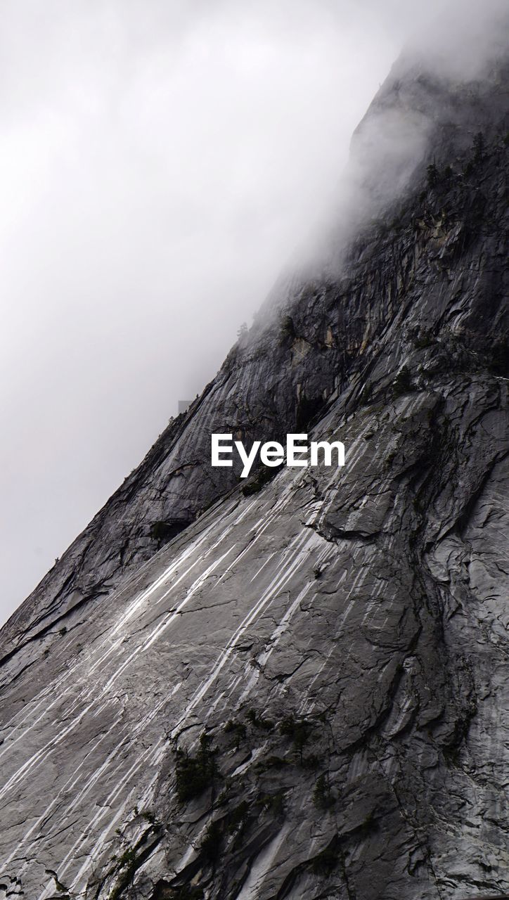 Low angle view of rocky wall against clouds