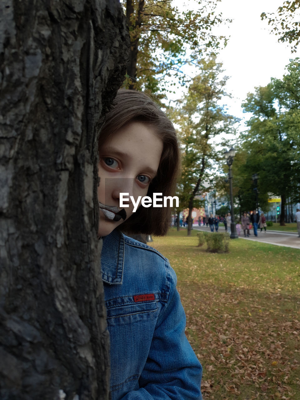 Portrait of woman with painted face by tree trunk