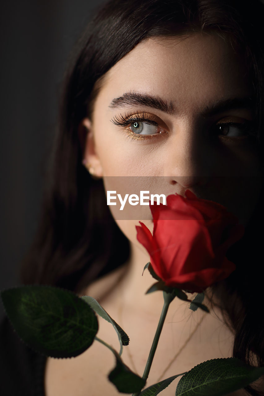 CLOSE-UP PORTRAIT OF WOMAN WITH RED ROSE