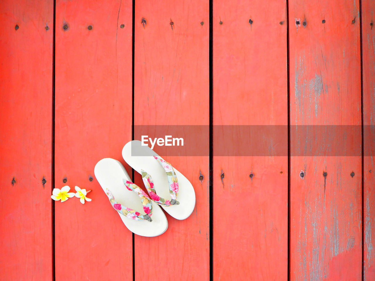 Directly above shot of flowers and slippers on red floorboard