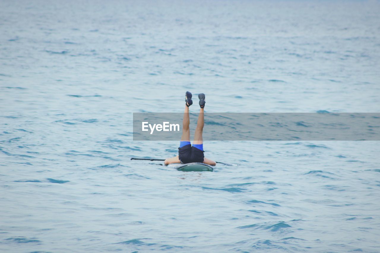 Low section of man with feet up paddleboarding in sea