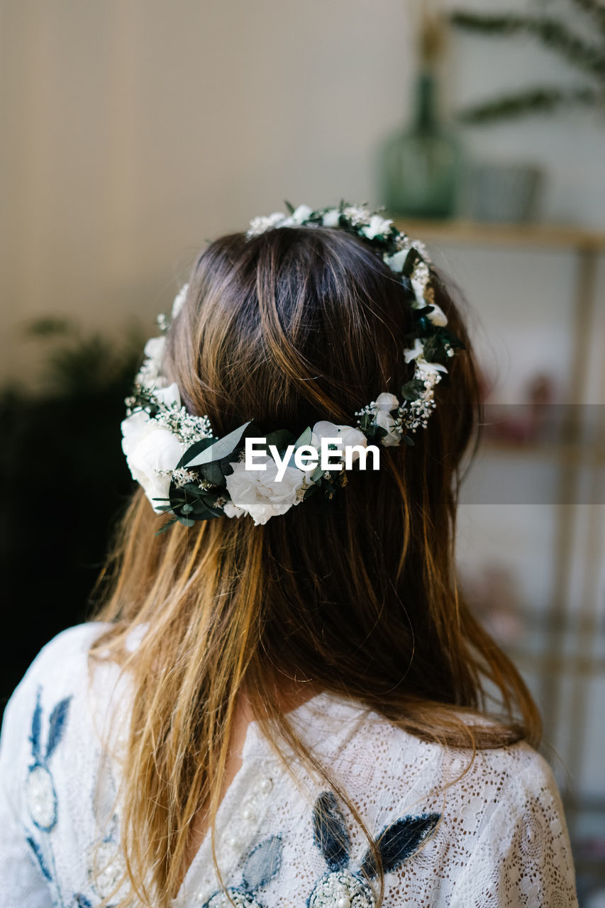 Back view of anonymous female wearing tender wreath with white rose flowers standing in flat