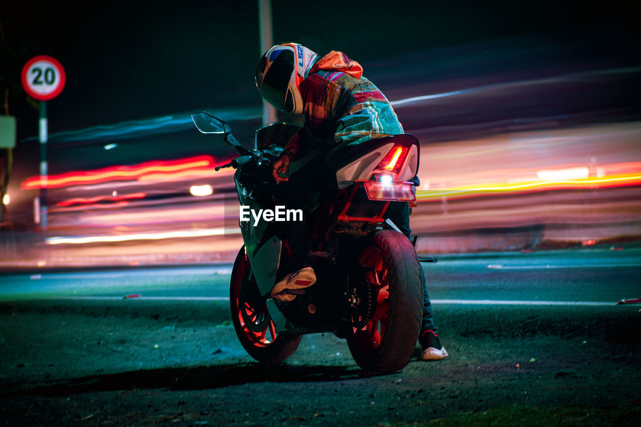rear view of man riding motorcycle on road at night