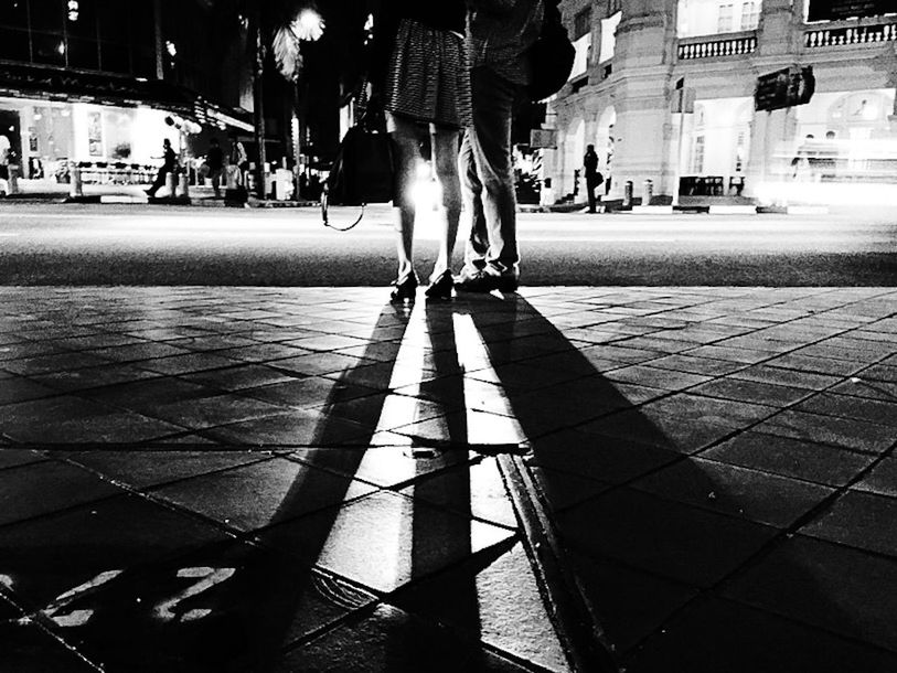 PEOPLE STANDING ON ILLUMINATED CITY STREET AT NIGHT